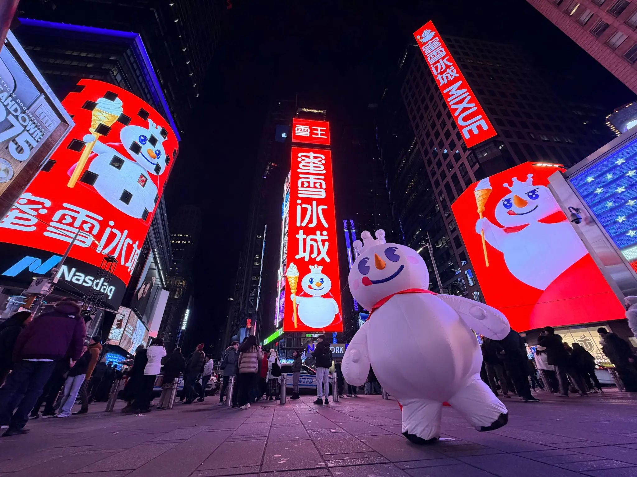 Painel de marca MIXUE exibido em Times Square Nova York à noite, mostrando o icônico mascote boneco de neve e logotipo da marca